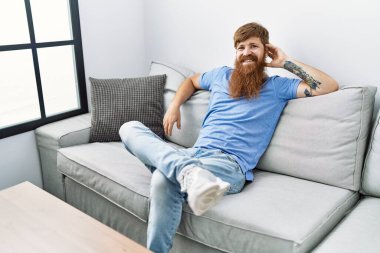 Genç İrlandalı mutlu gülümsüyor. Evdeki kanepede oturuyor..