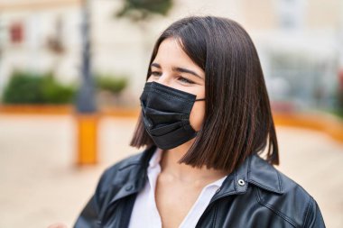 Genç, güzel, İspanyol bir kadın parkta maske takarak gülümsüyor.