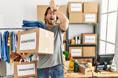 Handsome middle age man holding donations box for charity at volunteer stand surprised with hand on head for mistake, remember error. forgot, bad memory concept. 