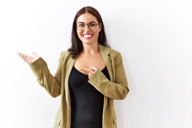 Genç esmer kadın izole edilmiş arka planda duruyor. Kameraya hayret ediyor ve gülümsüyor. Elleri ve parmaklarıyla işaret ediyor.. 