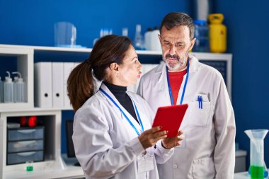 Orta yaşlı erkek ve kadın bilim adamları laboratuarda çalışan touchpad kullanıyorlar.