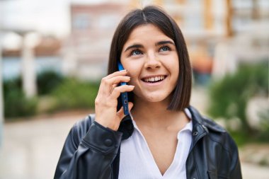 Genç, güzel İspanyol kadın gülümsüyor. Parktaki akıllı telefondan konuşuyor.