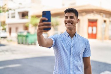 Genç İspanyol adam gülümsüyor. Sokakta akıllı telefonun yanında özçekim yapıyor.