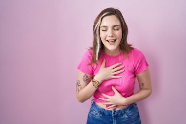 Blonde caucasian woman standing over pink background smiling and laughing hard out loud because funny crazy joke with hands on body. 