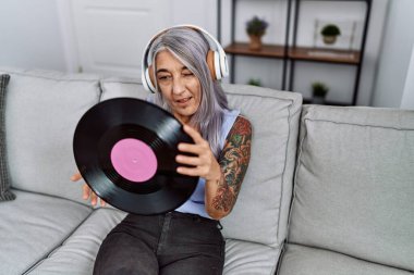 Orta yaşlı, kır saçlı, müzik dinleyen, elinde plak diski olan bir kadın. Kameraya seksi bir ifadeyle bakıyor. Neşeli ve mutlu bir yüzü var.. 