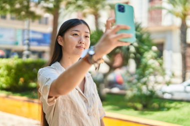 Parktaki akıllı telefonun yanında kendinden emin gülümseyen Çinli kadın.