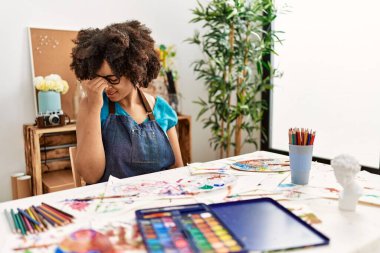 Sanat stüdyosunda afro saç boyalı güzel Afro-Amerikalı kadın. Burnu ve gözleri ovuşturmaktan yorulmuş, yorgun düşmüş ve başı ağrıyormuş. Stres ve hüsran kavramı. 