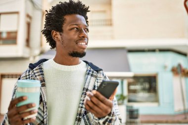 Afro saçlı yakışıklı siyah adam dışarıda mutlu gülümsüyor akıllı telefon kullanıyor.
