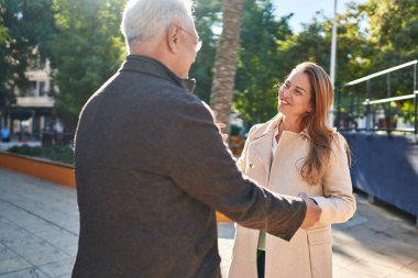 Orta yaşlı erkek ve kadın çift, parkta bir arada durarak gülümsüyor.