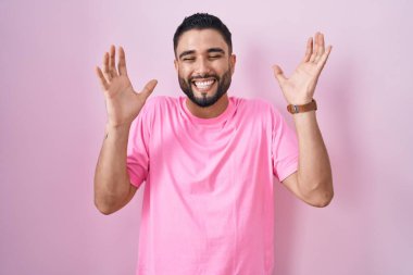 Pembe arka planda duran İspanyol genç adam başarının çılgınlığını kollarını kaldırarak ve gözleri kapalı heyecanla bağırarak kutluyor. Kazanan konsept 