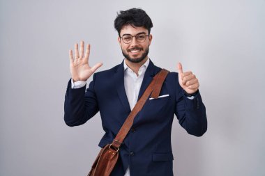 Hispanic man with beard wearing business clothes showing and pointing up with fingers number six while smiling confident and happy. 