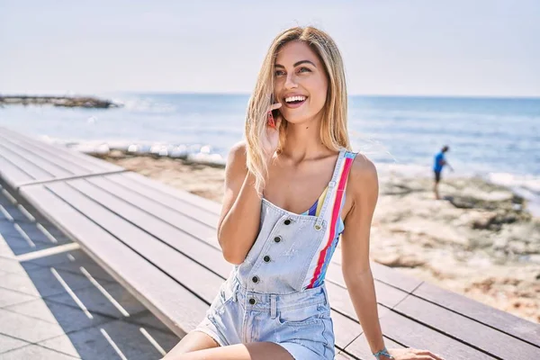 Молодая Блондинка Улыбается Счастливой Используя Смартфон Сидя Скамейке Пляже — стоковое фото