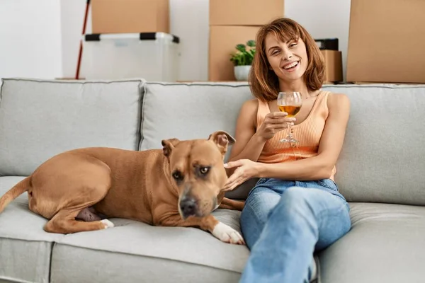 Young caucasian woman drinking wine sitting on sofa with dog at home