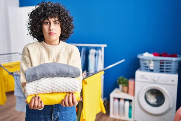 Young Brunette Woman Curly Hair Holding Clean Laundry Skeptic Nervous — Foto de Stock