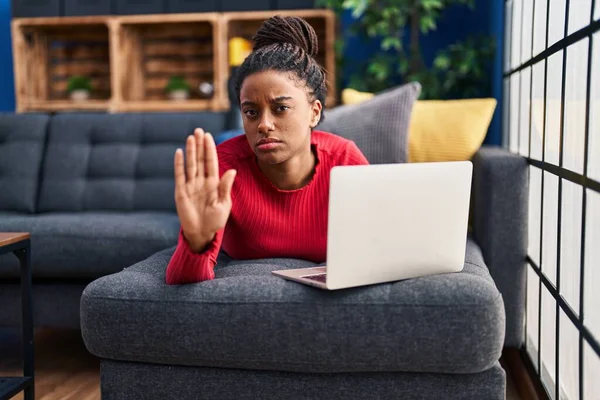 Young african american with braids working using computer laptop with open hand doing stop sign with serious and confident expression, defense gesture