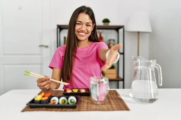 若いブルネットの女性は挨拶や歓迎として握手を提供する優しい笑顔箸を使用して寿司を食べる 成功したビジネス — ストック写真