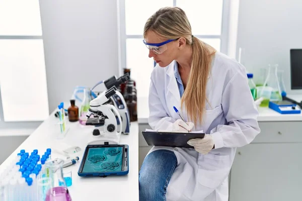 Young Blonde Woman Wearing Scientist Uniform Writing Clipboard Looking Embryion — Stockfoto
