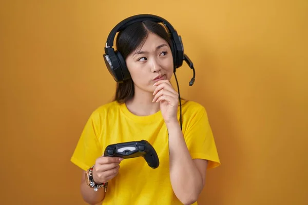 中国年轻女子手牵着下巴玩电子游戏控制器 思考问题 沉思的表情 脸上挂着沉思的笑容 怀疑概念 — 图库照片