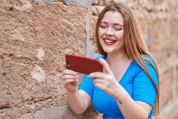 Młoda Ruda Kobieta Uśmiecha Się Pewnie Oglądając Wideo Smartfonie Odizolowanym — Zdjęcie stockowe
