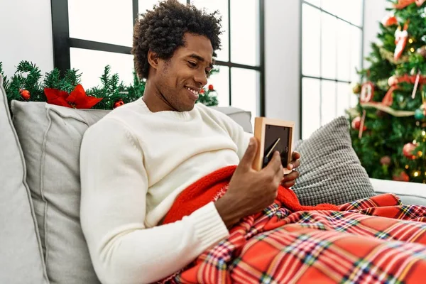 Joven Afroamericano Hombre Sosteniendo Foto Sentado Sofá Por Árbol Navidad — Foto de Stock