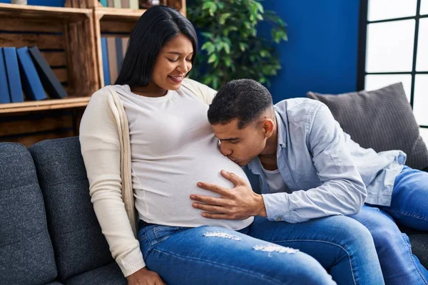 Jovem Casal Latino Esperando Bebê Beijando Barriga Sentado Sofá Casa — Fotografia de Stock