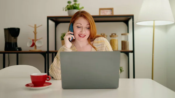 Молодая Рыжая Женщина Использует Ноутбук Разговаривает Смартфоне Дома — стоковое фото