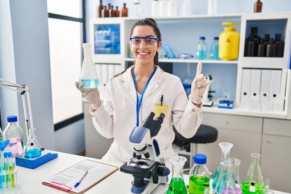 Hispanic woman working at scientist laboratory smiling with an idea or question pointing finger with happy face, number one
