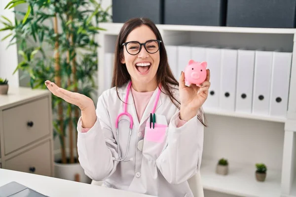 幸せな笑顔で達成を祝う貯金箱を保持している若い医師の女性と受賞式とともに上げ手 — ストック写真