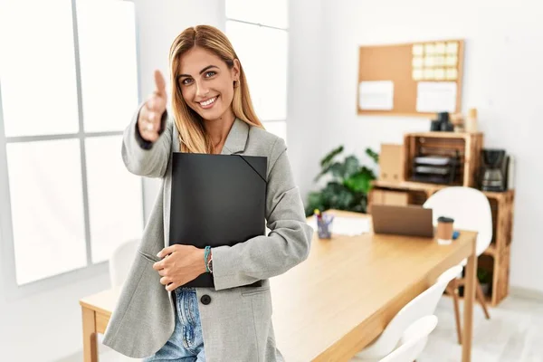 Blonde business woman at the office smiling friendly offering handshake as greeting and welcoming. successful business.