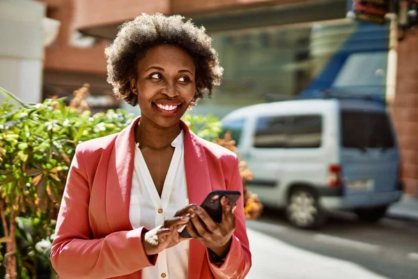 Beautiful business african american woman with afro hair smiling happy and confident outdoors at the city using smarpthone