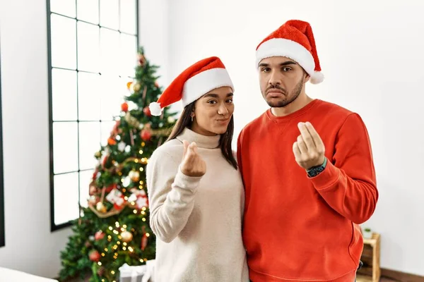 クリスマスツリーのそばに立つ若いヒスパニック系のカップル手でお金のジェスチャーをし 給与支払いを求め 億万長者のビジネス — ストック写真