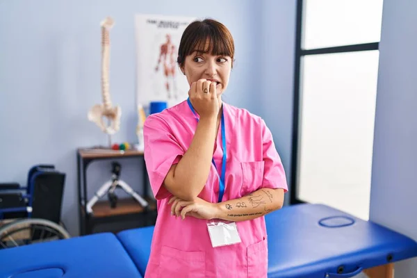 リハビリテーションクリニックで働く若いブルネットの女性は 口の中で爪をかむ上で手でストレスと緊張しています 不安の問題 — ストック写真