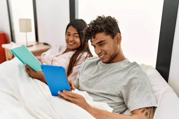 Unga Latinska Par Läser Bok Med Pekplatta Sitter Sängen Sovrummet — Stockfoto