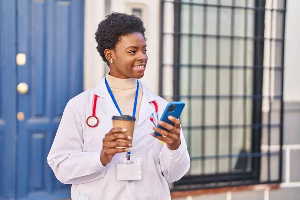 African American Woman Wearing Doctor Uniform Using Smartphone Drinking Coffee — Photo