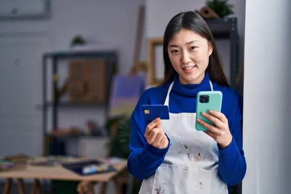 Chinese woman artist using smartphone and credit card at art studio