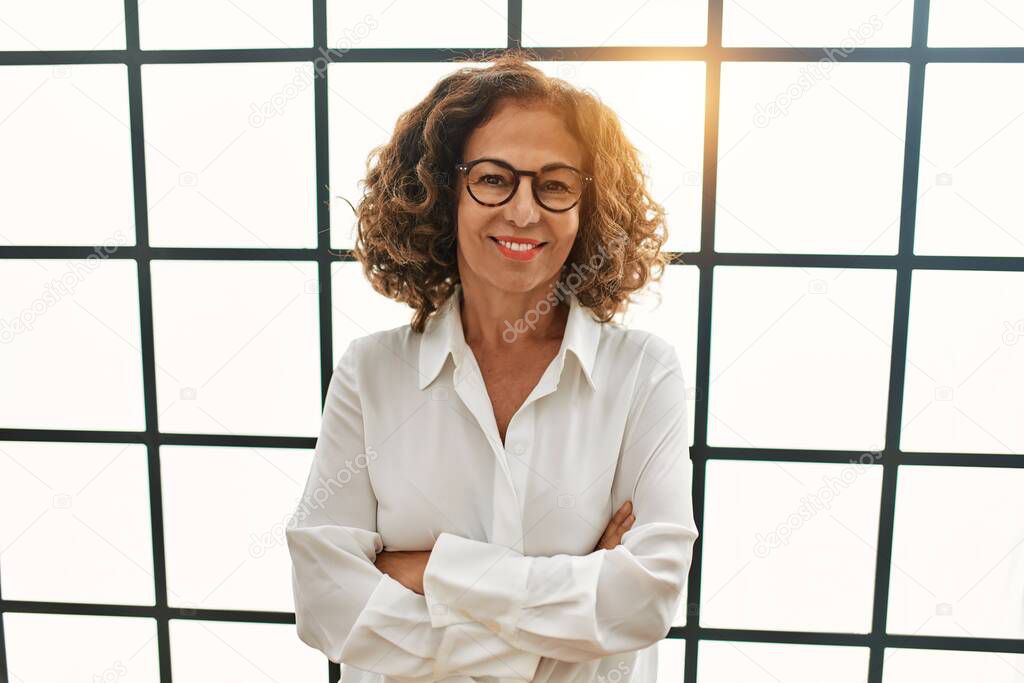 Middle age hispanic woman smiling confident with arms crossed gesture at office