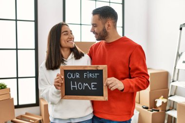 Genç Latin çift mutlu bir şekilde gülümsüyor. İlk ev mesajımızla birlikte ellerinde tahtayla..