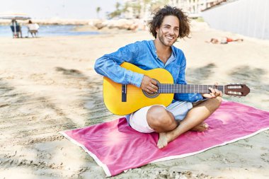 Genç İspanyol bir adam kumsalda oturmuş klasik gitar çalıyor..