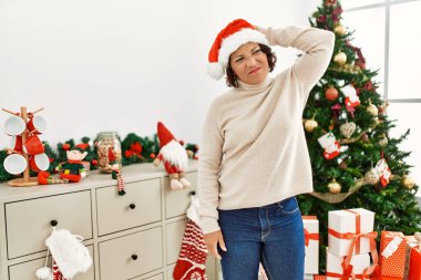 Orta yaşlı İspanyol kadın noel ağacının yanında duruyor. Soruları merak ediyor ve şaşırıyor. Şüpheyle kararsız, kafa kafaya düşünerek. Düşünceli kavram. 