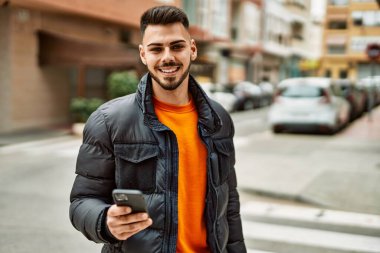 Yakışıklı, sakallı, mutlu ve kendine güvenen, akıllı telefon kullanan, kışlık palto giyen bir İspanyol.