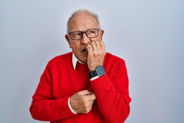 Senior man with grey hair standing over isolated background looking stressed and nervous with hands on mouth biting nails. anxiety problem. 