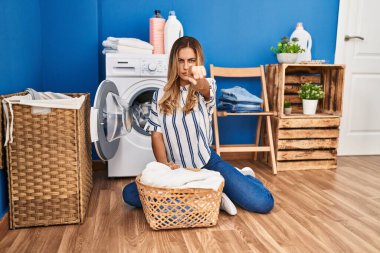 Çamaşırlarını yıkayan genç sarışın kadın evde kamerayı işaret ediyor ve sen kendinden emin bir şekilde ciddi görünüyorsun. 