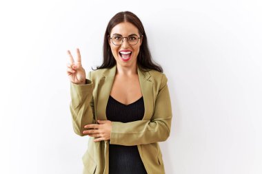 Genç esmer kadın izole edilmiş arka planda duruyor. Gülümsüyor ve kameraya göz kırpıyor. Parmaklarıyla zafer işareti yapıyor. İki numara.. 