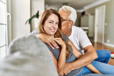 Orta yaşlı İspanyol çift mutlu bir şekilde gülümsüyor ve evdeki kanepede oturup sarılıyorlar..