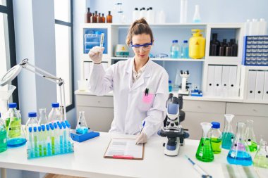 Young woman wearing scientist uniform analysing herb at laboratory
