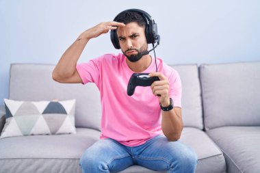 Kanepede oturmuş video oyunu oynayan Latin asıllı genç adam alında bir sorun olduğu için endişeli ve stresli. Kriz için endişeli. 
