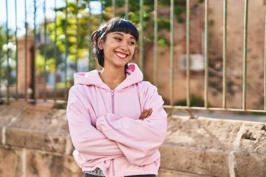 Kendine güvenen genç bir kadın caddede kollarını kavuşturmuş duruyor.