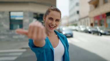 Young woman smiling confident doing coming gesture with finger at street