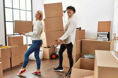 Mutlu bir şekilde gülümseyen genç çift yeni evlerinde karton kutular tutuyor..