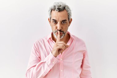 Orta yaşlı İspanyol bir adam izole edilmiş arka planda duruyor ve parmakları dudaklarında sessiz olmak istiyor. sessizlik ve gizli konsept. 